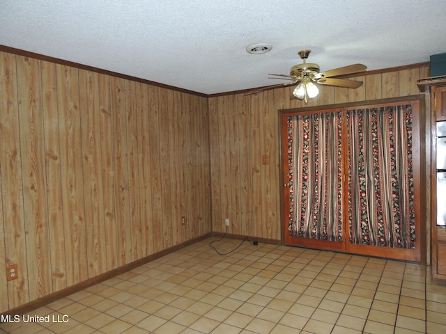 spare room with ceiling fan, a textured ceiling, crown molding, and wood walls