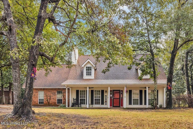 new england style home with roof with shingles, brick siding, a front lawn, and a chimney