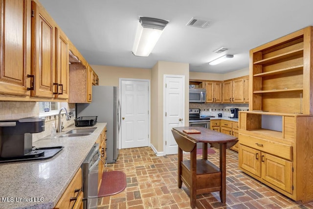 kitchen featuring light stone counters, stainless steel appliances, a sink, visible vents, and tasteful backsplash