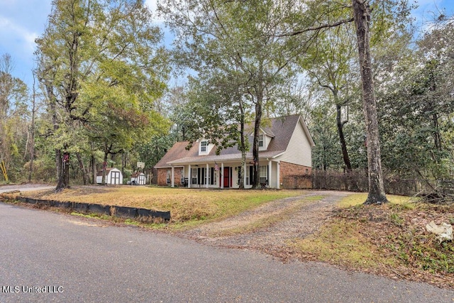 cape cod house featuring an outbuilding, driveway, a shed, and brick siding