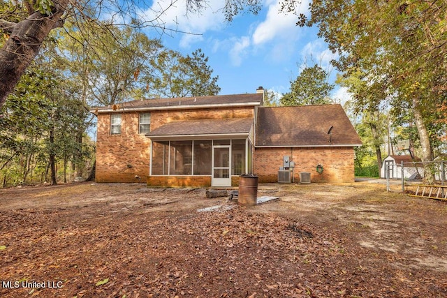 rear view of property with an outbuilding, a chimney, a storage unit, central AC unit, and a sunroom