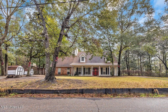 cape cod home with a storage shed, a front yard, covered porch, and an outbuilding