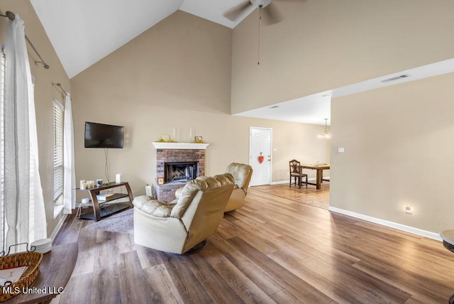 living room with a brick fireplace, visible vents, baseboards, and wood finished floors