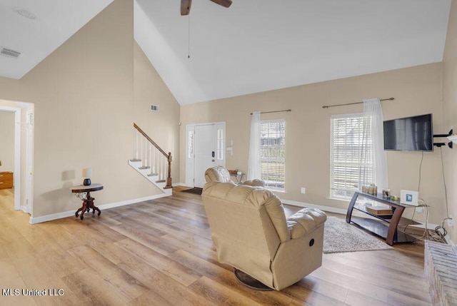 living area featuring high vaulted ceiling, visible vents, baseboards, stairs, and light wood finished floors