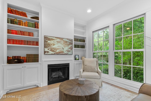 living area featuring crown molding, built in shelves, and light hardwood / wood-style floors