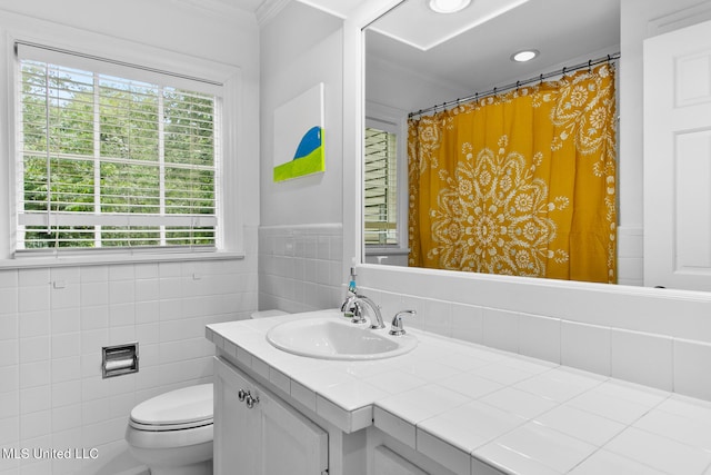 bathroom featuring toilet, ornamental molding, vanity, and tile walls