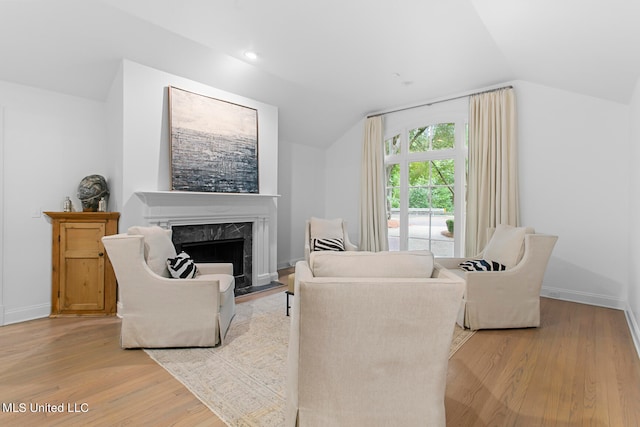 living room featuring lofted ceiling, a premium fireplace, and light hardwood / wood-style floors