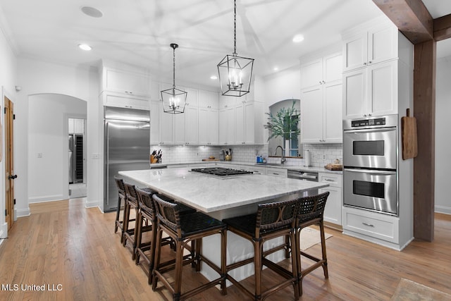 kitchen with white cabinetry, a kitchen bar, stainless steel appliances, light hardwood / wood-style floors, and a center island