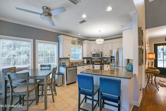 kitchen with hanging light fixtures, ceiling fan, light tile patterned floors, appliances with stainless steel finishes, and white cabinetry