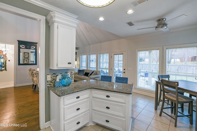 kitchen with white cabinets, light tile patterned floors, ceiling fan, and dark stone counters