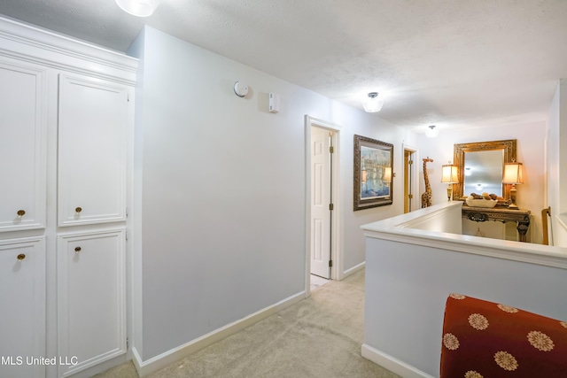 corridor featuring a textured ceiling and light carpet