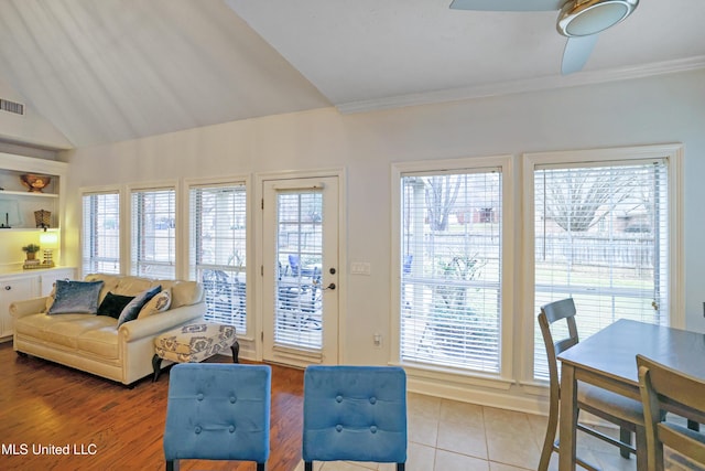 tiled living room featuring built in shelves, ceiling fan, vaulted ceiling, and ornamental molding