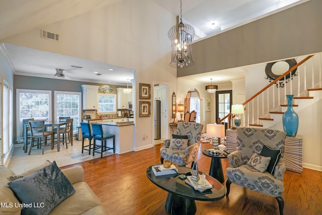 living room with ceiling fan with notable chandelier, high vaulted ceiling, and light hardwood / wood-style flooring