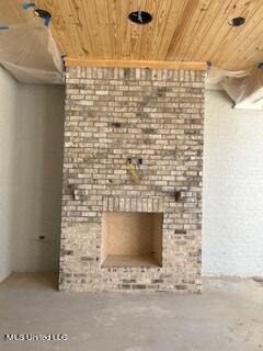 unfurnished living room featuring concrete flooring, wood ceiling, and a brick fireplace