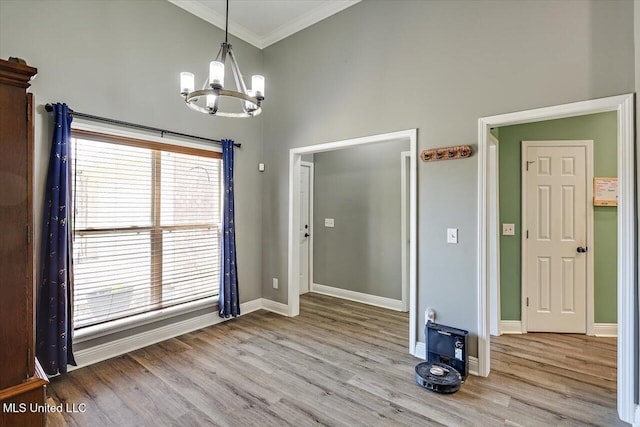 unfurnished dining area with ornamental molding, light wood finished floors, a high ceiling, and a notable chandelier