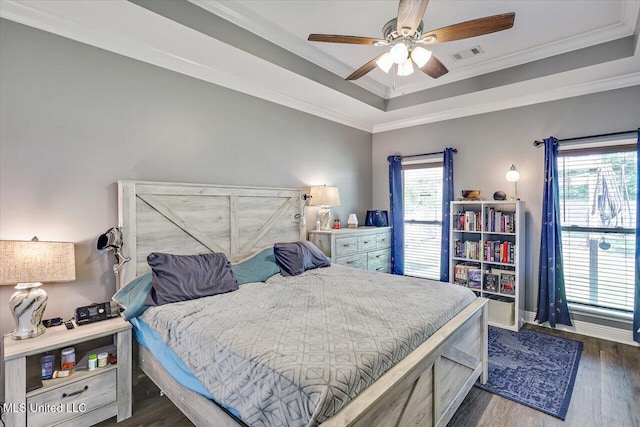 bedroom featuring visible vents, crown molding, wood finished floors, baseboards, and a tray ceiling