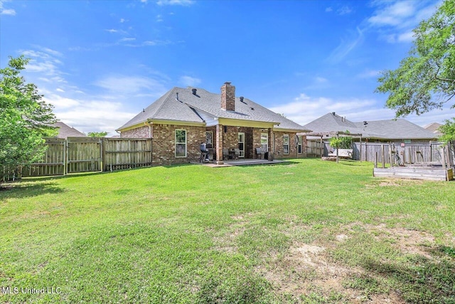 rear view of house with a fenced backyard, a chimney, a lawn, and brick siding