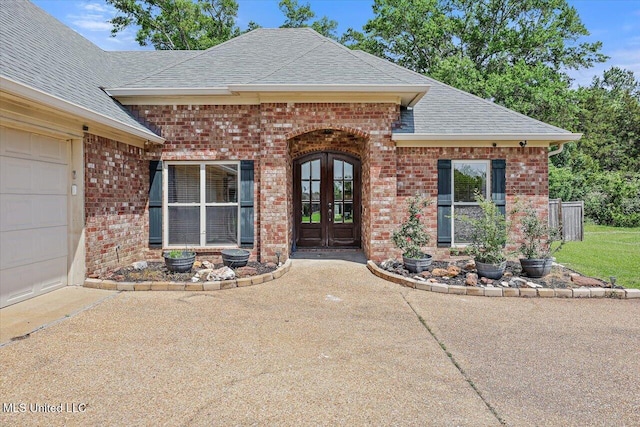 view of exterior entry featuring brick siding, an attached garage, french doors, and a shingled roof