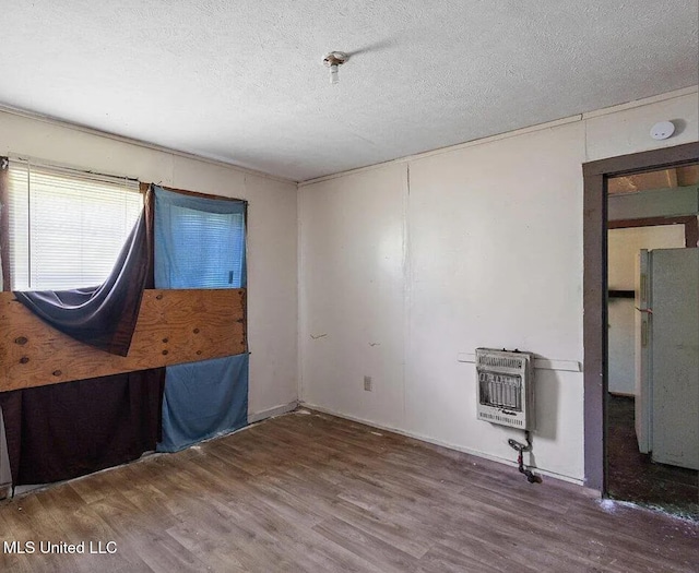 spare room featuring heating unit, hardwood / wood-style floors, and a textured ceiling