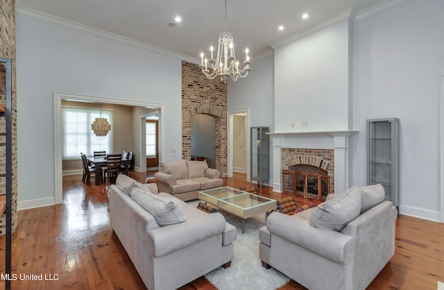 living room featuring a high ceiling, hardwood / wood-style flooring, ornamental molding, an inviting chandelier, and a fireplace