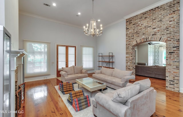 living room featuring a high ceiling, light hardwood / wood-style floors, ornamental molding, a brick fireplace, and ceiling fan with notable chandelier