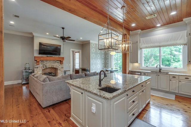 kitchen with an island with sink, white cabinets, sink, and pendant lighting