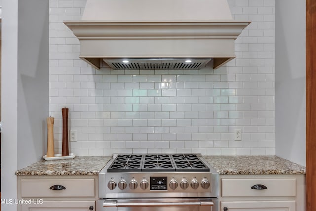 kitchen featuring custom range hood, stainless steel stove, light stone counters, and backsplash