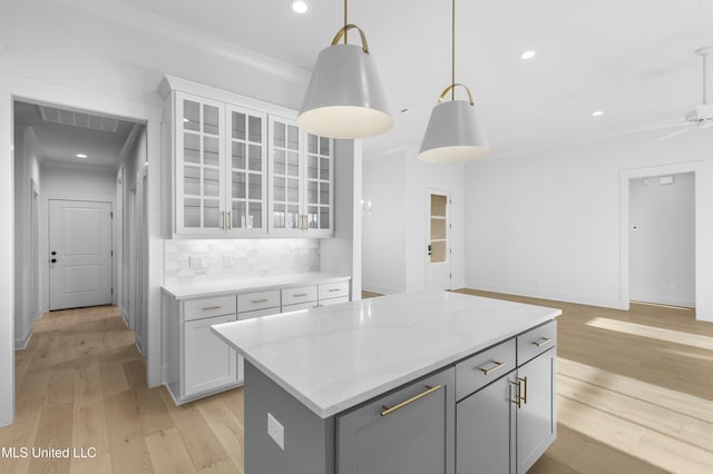 kitchen featuring gray cabinetry, decorative light fixtures, light hardwood / wood-style flooring, a kitchen island, and backsplash