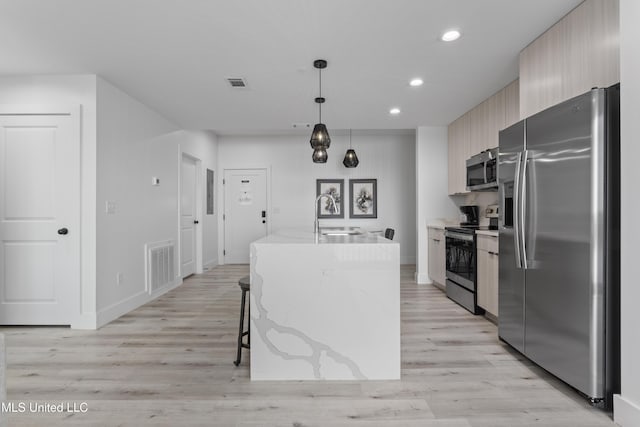 kitchen with a kitchen bar, decorative light fixtures, appliances with stainless steel finishes, a kitchen island with sink, and light hardwood / wood-style floors