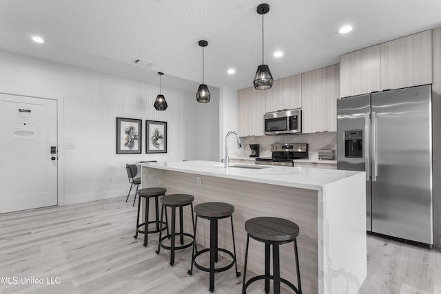 kitchen featuring sink, a kitchen island with sink, hanging light fixtures, stainless steel appliances, and light stone counters