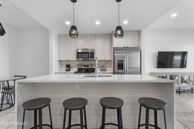 kitchen featuring light stone counters, appliances with stainless steel finishes, an island with sink, and hanging light fixtures