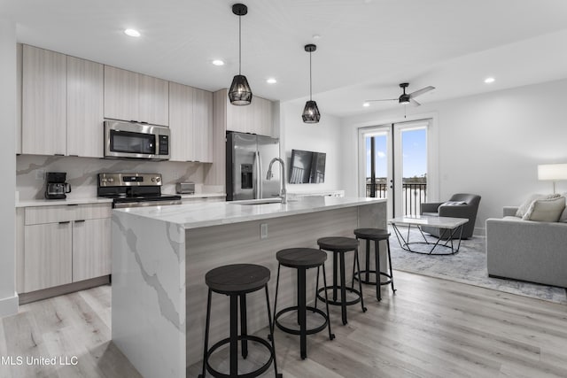 kitchen featuring light stone counters, appliances with stainless steel finishes, decorative light fixtures, and a center island with sink