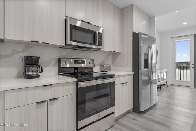 kitchen with tasteful backsplash, light wood-type flooring, light brown cabinets, and appliances with stainless steel finishes