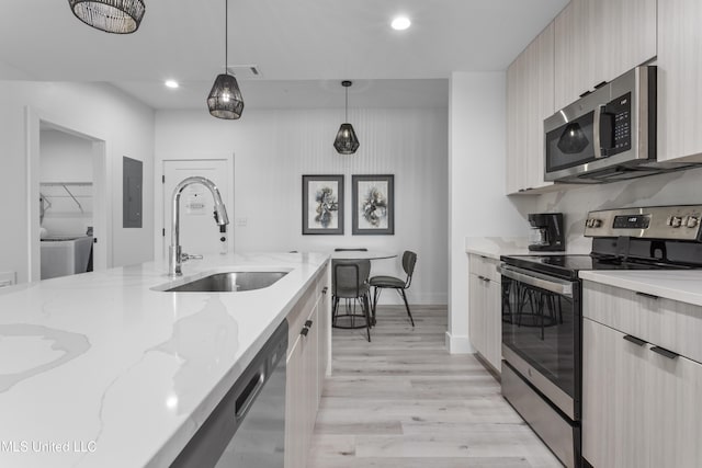 kitchen with sink, hanging light fixtures, stainless steel appliances, light stone countertops, and light hardwood / wood-style flooring