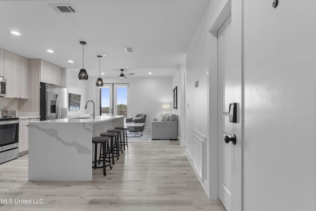 kitchen with pendant lighting, a center island with sink, light hardwood / wood-style floors, and appliances with stainless steel finishes