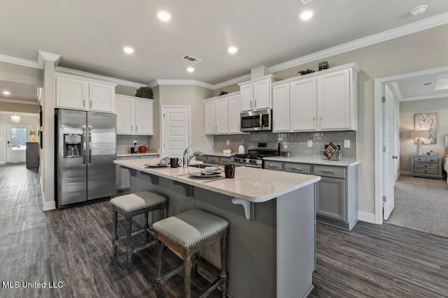 kitchen with appliances with stainless steel finishes, a center island with sink, dark hardwood / wood-style floors, white cabinetry, and a breakfast bar area