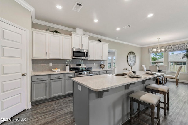 kitchen featuring a kitchen island with sink, sink, dark hardwood / wood-style floors, appliances with stainless steel finishes, and a breakfast bar area