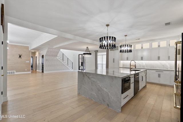 kitchen with wall oven, hanging light fixtures, a kitchen island with sink, white cabinets, and light stone counters