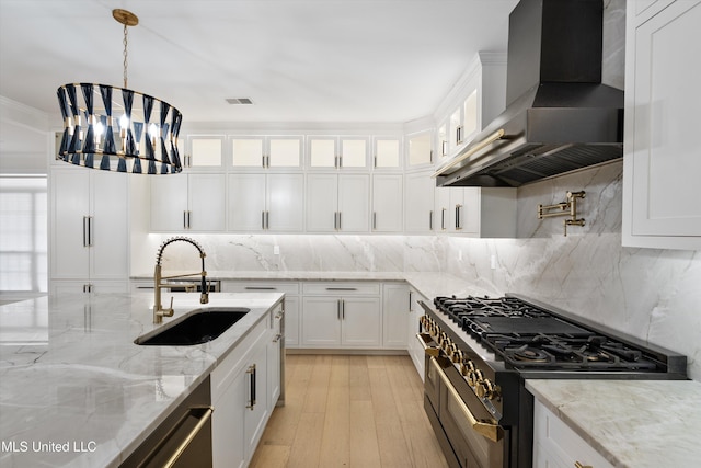 kitchen featuring sink, white cabinetry, light stone counters, range with two ovens, and ventilation hood