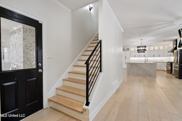 foyer with sink, light wood-type flooring, a chandelier, and crown molding