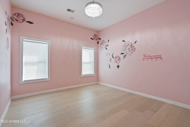 empty room featuring a wealth of natural light, light hardwood / wood-style flooring, and a chandelier