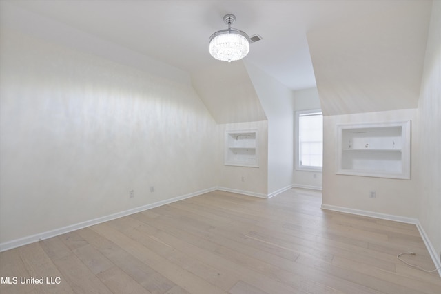 additional living space with built in features, light hardwood / wood-style flooring, and an inviting chandelier