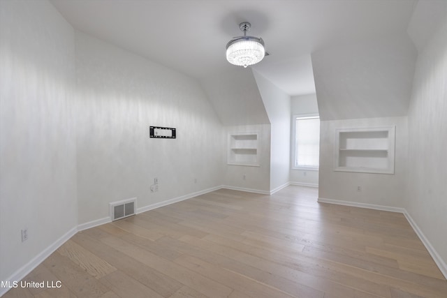 bonus room with lofted ceiling, built in features, an inviting chandelier, and light wood-type flooring