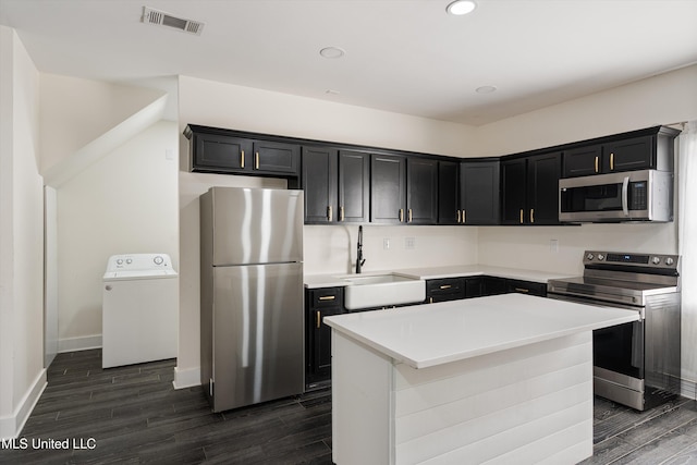 kitchen with washer / dryer, a center island, appliances with stainless steel finishes, sink, and dark wood-type flooring