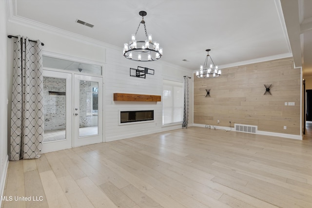 unfurnished living room featuring crown molding, light wood-type flooring, a large fireplace, wood walls, and an inviting chandelier