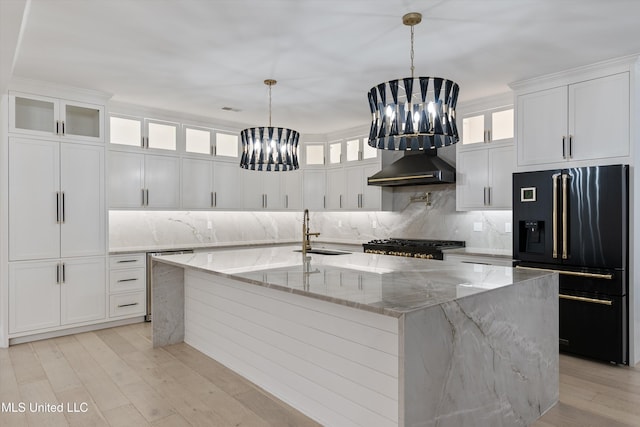 kitchen featuring high end black fridge, wall chimney range hood, sink, a large island, and a chandelier