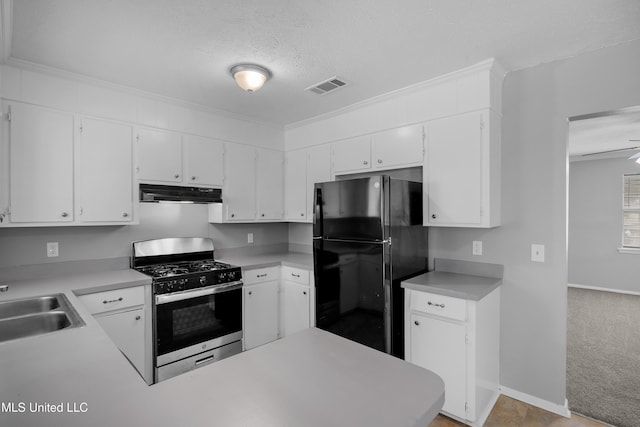 kitchen featuring light countertops, freestanding refrigerator, gas range, under cabinet range hood, and visible vents