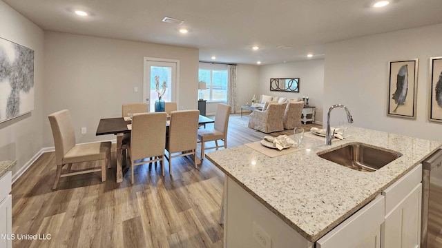 kitchen featuring sink, light stone counters, light hardwood / wood-style flooring, a kitchen island with sink, and white cabinets