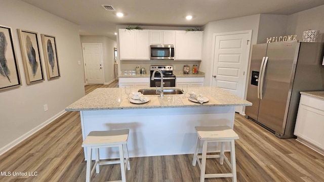 kitchen with a breakfast bar, a kitchen island with sink, sink, appliances with stainless steel finishes, and white cabinetry