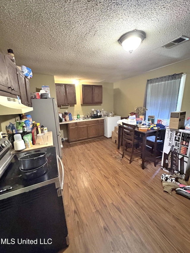 kitchen with a textured ceiling, electric range, under cabinet range hood, light wood-style floors, and visible vents